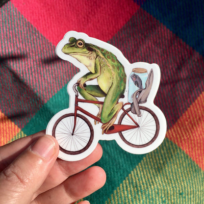 Bicycle Frog sticker held in a hand over a bright red, green and orange tartan blanket in warm sunlight