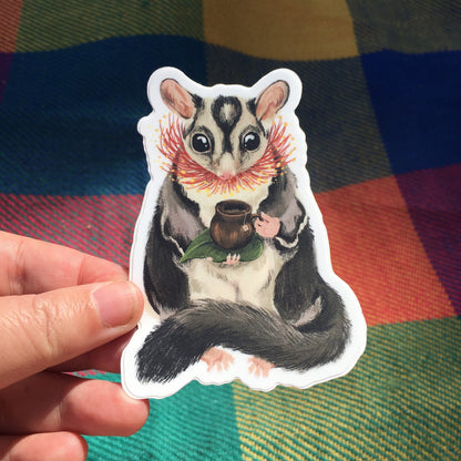 Sugar Glider Teatime sticker held in a hand over a colourful tartan blanket in warm sunlight